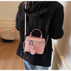 Close-up of a pink box-shaped crossbody bag worn over a stylish black blazer.