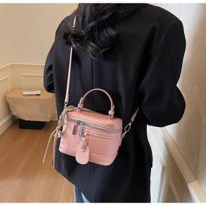 Detail of a pink leather box handbag worn as a crossbody bag with a black blazer
