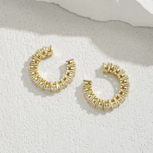 Dettaglio di orecchini ear cuff placcati in oro con zirconi su uno sfondo bianco