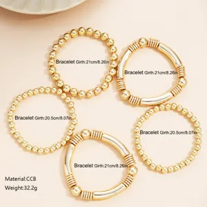 Detail van een set van vijf goudkleurige stapelbare kralen- en buisarmbanden.