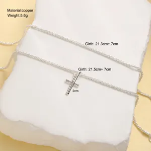 Detail view of a minimalist silver cross pendant anklet set on a white stone background.