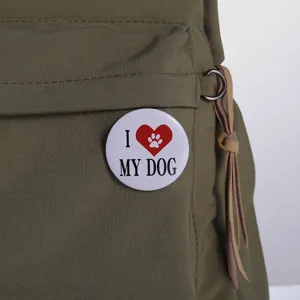 White round tinplate brooch pin with 'I love my dog' heart paw design on a green bag