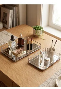 Twee rechthoekige zilveren spiegeldienbladen met luxe cosmetica op een houten tafel.