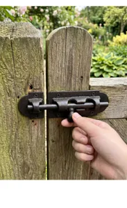Close-up of hand operating a rustic cast iron sliding latch bolt on a wooden gate