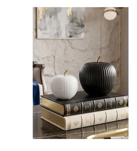 Close-up of elegant black and white ribbed ceramic apple ornaments on stacked books.