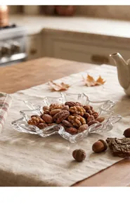 Detalle de un frutero de vidrio transparente en forma de hoja de arce con nueces.