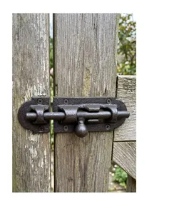 Heavy-duty cast iron sliding door bolt latch installed on a rustic wooden gate.
