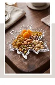 Primer plano de un plato de vidrio con forma de hoja de arce y frutos secos variados.