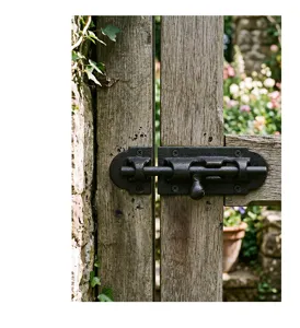 Rustic black cast iron sliding bolt latch installed on a weathered wooden garden gate