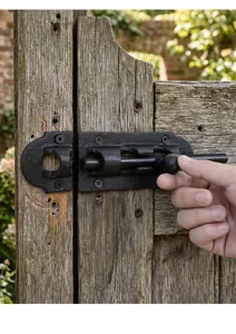 Close-up of a rustic black cast iron sliding bolt latch installed on a wooden gate