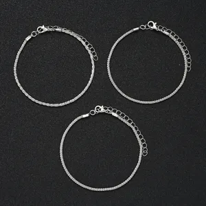 Detail of three shimmering silver minimalist anklets on a dark textured surface