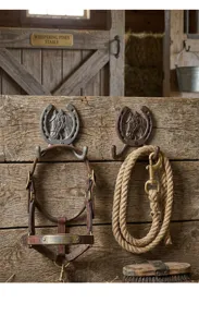 Detailansicht rustikaler Gusseisen-Hufeisenhaken mit Pferdekopf auf Holzstallwand.