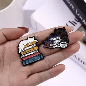 Nahaufnahme von niedlichen Emaille-Pins mit Katzen- und Buchmotiven in der Hand präsentiert