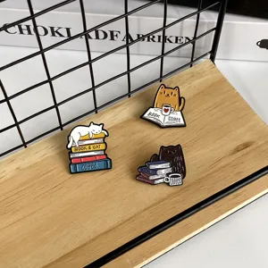Set aus drei Emaille-Pins mit Katzen- und Buchmotiven auf einem Holzständer im Detail.