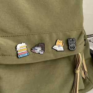 Nahaufnahme von vier Emaille-Anstecknadeln mit Katzen und Büchern auf einem Rucksack