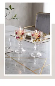 Paar elegante tulpenförmige Kristallglas-Kerzenhalter mit getrockneten Blüten auf Marmortisch