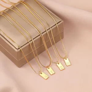 Primer plano de collares de cadena de caja dorada con colgantes de letras grabadas.