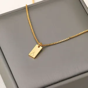 Primer plano de un collar de cadena box dorada con un colgante grabado de la letra A.