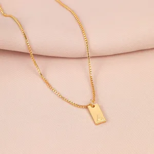 Primer plano de un collar de cadena box dorada con colgante cuadrado letra A grabada.