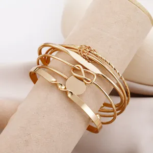 Close-up detail of a five-piece set of gold-toned geometric and knotted open bangles