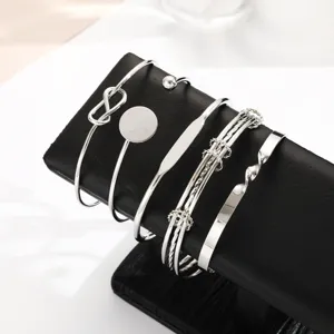 Detailed view of five silver-toned minimalist open cuff bracelets on a display stand