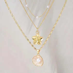 Macro detail of gold layered necklace featuring a shell pendant with pearl and flower charm