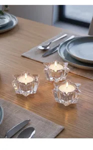 Drie stervormige glazen kandelaars met brandende theelichtjes op een houten tafel