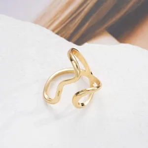 Close-up of a minimalist gold irregular wavy open ring on a white stone background.