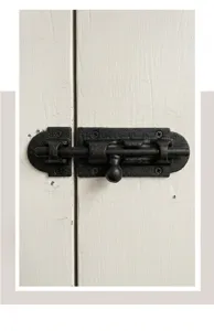 Close-up view of a rustic black cast iron door bolt latch installed on a white wood door