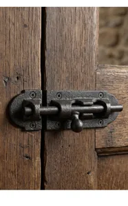 Close-up detail of a vintage cast iron sliding bolt latch on a rustic wooden door.