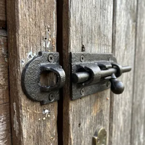 Rustic black cast iron sliding door bolt latch installed on a weathered vintage wood door