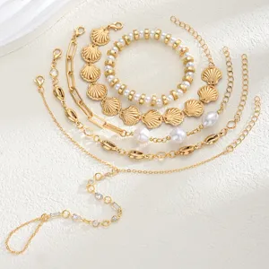 Detalle de conjunto de pulseras de conchas doradas y perlas con elegante cadena de mano