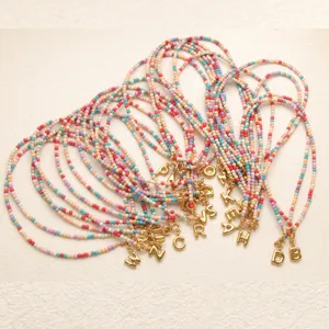 Perles colorees en detail presentant des charms lettres dorees et collier style boheme closeup.