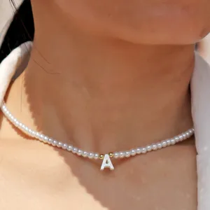 Gros plan sur le collier ras de cou en perles avec pendentif lettre en coquillage et détails dorés.