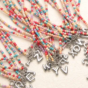 Gros plan détail de collier bohème en perles colorées avec pendentif lettre en acier inoxydable.