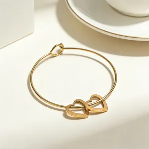 Nahaufnahme eines goldenen Edelstahl-Armreifs mit doppelten Herzanhängern im Detail.