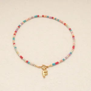Collier bohème en perles colorées avec pendentif lettre F dorée et fermoir délicat.