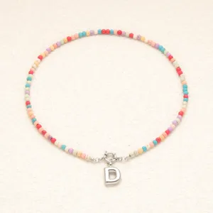 Gros plan détail du collier bohème en perles colorées avec pendentif argenté lettre D.