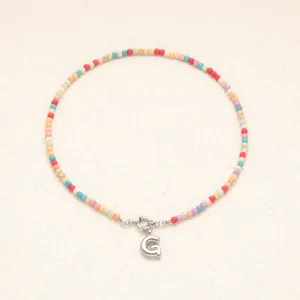 Gros plan détaillé du collier de perles colorées style bohème avec pendentif lettre en acier inox.