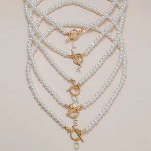 Élégant collier de perles avec fermoir OT doré et pendentifs lettres scintillants.