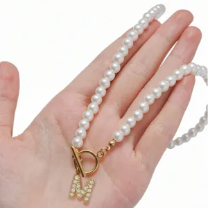 Gros plan détaillé du collier de perles élégant avec fermoir OT doré et pendentif lettre M.