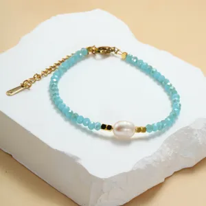 Close-up van blauwe kristalen kralenarmband met zoetwaterparel en gouden kettingdetails.
