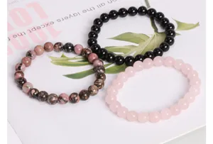 Nahaufnahme von drei Perlenarmbändern in Schwarz, Rosa und Steinoptik auf weißem Papier.