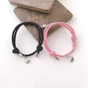 Détail de bracelets tressés magnétiques pour couples, corde noire et rose avec jolis pendentifs.