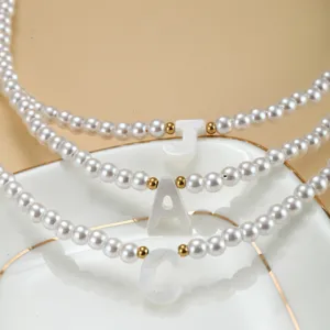 Détail du collier de perles lettre, pendentif coquillage nacré sur chaîne délicate.