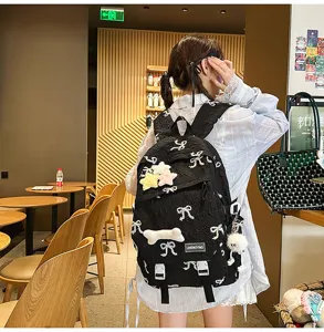 Detalle de una linda mochila acolchada negra con bordado de lazo blanco y colgantes