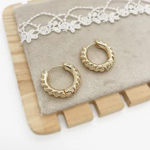 Macro view showing the intricate twisted texture of gold-plated hoop earrings on velvet