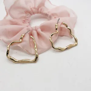 Macro detail shot of irregular gold heart-shaped earrings with a shiny metallic finish