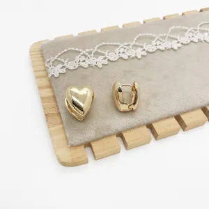 Detailed macro view of golden heart-shaped hoop earrings on a grey velvet stand