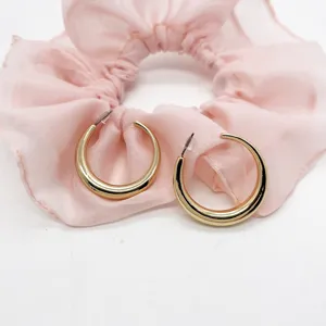 Close-up of elegant chunky gold hoop earrings resting on soft pink ruffled fabric decor